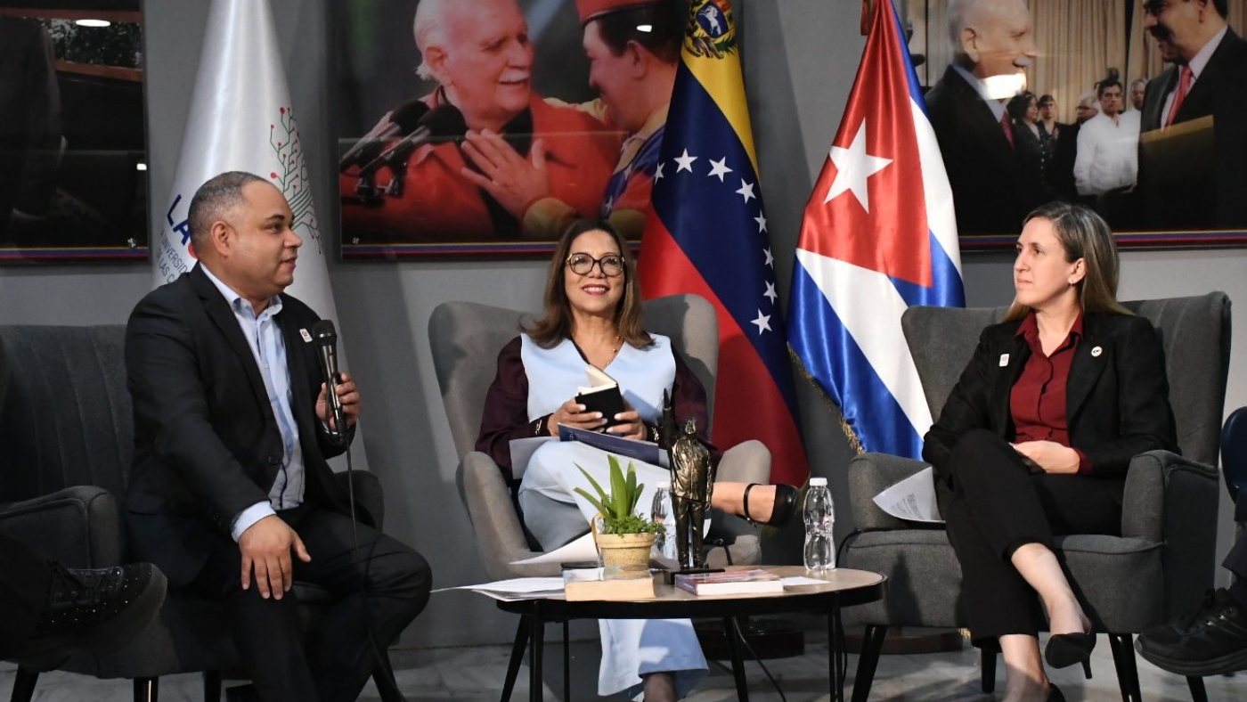 Las autoridades y ponentes durante la Sesión Especial de la Cátedra Internacional Hugo Chávez en LAUICOM, con las banderas de Venezuela y Cuba de fondo.