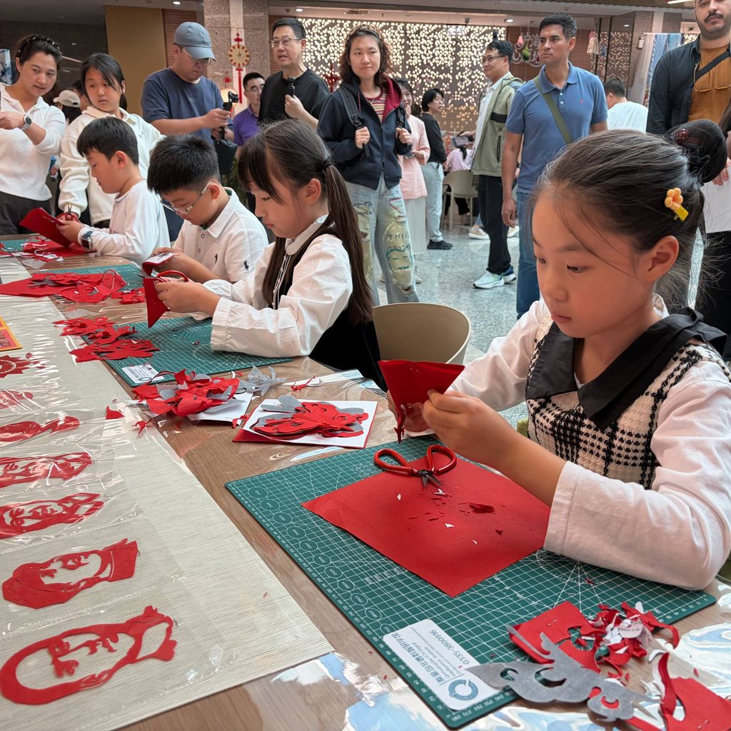 Niños de Qinhuangdao haciendo manualidades con adultos en el fondo